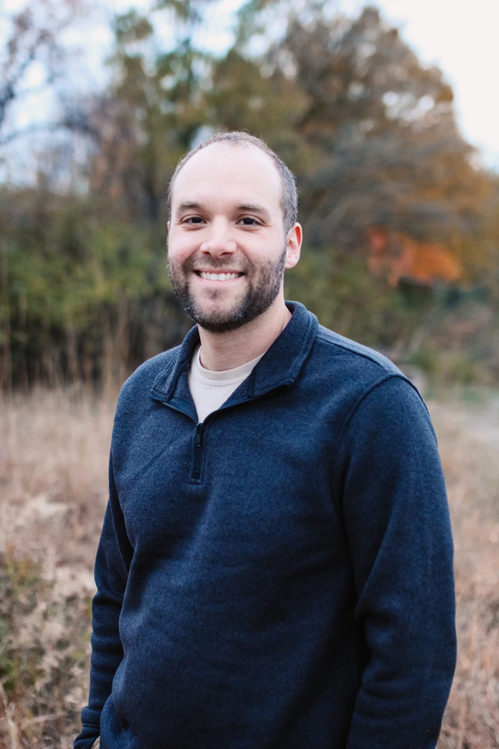 Ian Hett, owner of Hett Tech Solutions, smiling outdoors in a navy quarter-zip sweater